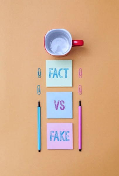 Text sign showing Fact Vs Fake. Conceptual photo Rivalry or products or information originaly made or imitation Coffee cup blank colored sticky note two ballpoints clips yolk background. — Stock Photo, Image