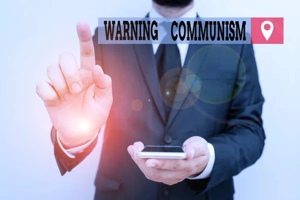 Writing note showing Warning Communism. Business photo showcasing economic system where the group owns the production Male human wear formal work suit hold smartphone using hand.