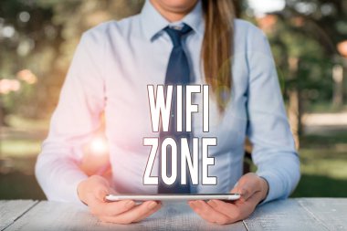 Wifi Zone 'u gösteren bir not yazıyorum. İş fotoğrafı tanıtımı, yüksek hızlı kablosuz internet ve ağ bağlantıları sunar. Masa başında oturan ve cep telefonu tutan kadın iş adamı.