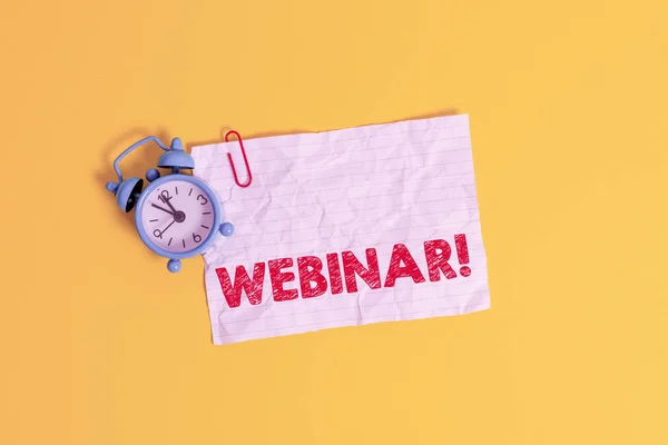 Signo de texto que muestra Webinar. Foto conceptual: un seminario u otra presentación que tiene lugar en Internet Clip de reloj despertador de metal en blanco hoja de nota triturada fondo de color . — Foto de Stock