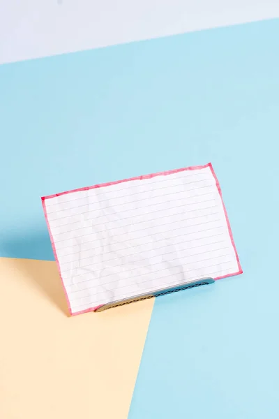 Paper sheet placed tilted on a buffer wire with a soft pastel backdrop. Notepaper on the edge of empty plain multi colours table. Artistic way of arranging flat lays photography — 图库照片