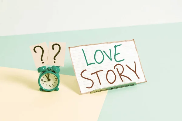 Texte manuscrit Love Story. Concept signifiant que c'est quelque chose comme un roman ou un film sur une histoire d'amour Mini réveil de taille à côté d'une feuille de papier placée inclinée sur fond pastel . — Photo
