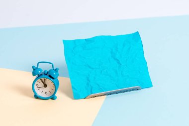 Kağıt bir çarşafın yanına yerleştirilmiş küçük bir çalar saat. Boş sade çok renkli masa arkaplanının kenarındaki not kağıdı. Dairenin sanatsal düzenleme yöntemi fotoğrafçılıktır.