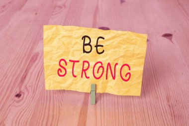 Kavramsal el yazısı Güçlü Olun 'u gösteriyor. Hayattaki büyük koşullara ya da baskıya dayanabilen iş fotoğrafı metni. Ahşap zemin zemin arka plan yeşil çamaşır mandalı oyuk ofisi..