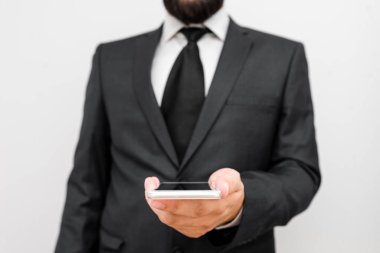 Sakallı bir erkek resmi iş kıyafetleri giyer yüksek teknoloji akıllı telefon cihazı taşır. İş elbisesi giymiş bir adam ve kravatlı küçük cep telefonlu bir adam tek elini kullanıyor.