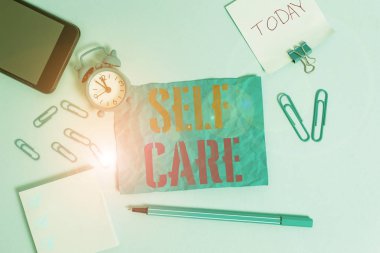 Kelimelerle yazılan Öz Bakım. Eylem koruma ya da iyileştirme uygulaması için iş konsepti. Kendi sağlık alarmlı saat klipsleri. Akıllı telefon lastiği işaretleyici renkli arkaplan.