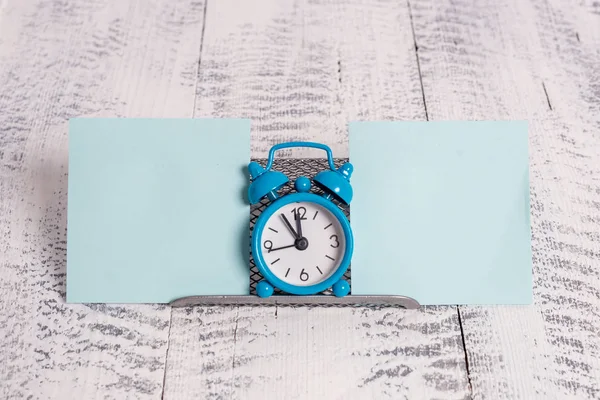 Mini-Wecker in blauer Farbe, der die Zeit zwischen zwei blauen Zetteln anzeigt. klassische kleine Uhr, die über einem Pufferdraht inmitten von Notizpapier steht — Stockfoto