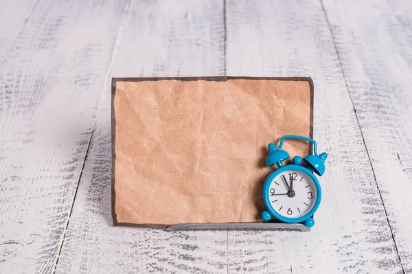 Mini blauwe kleur wekker om te laten zien tijd geplaatst gekanteld in de voorkant van een bruin oud briefpapier. Klassiek horloge boven een bufferdraad voor notatiepapier — Stockfoto