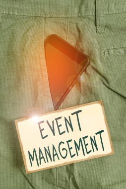 Etkinlik Yönetimi el yazısı metni. Resmi iş pantolonu içindeki akıllı telefon aygıtı, nota kağıdının yanındaki ön cebin planlama ve analiz işi anlamına gelir..