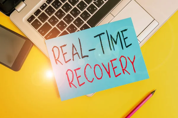 Writing note showing Real Time Recovery. Business photo showcasing maximum time period in which recent data can recover Metallic laptop small paper sheet pencil smartphone colored background.