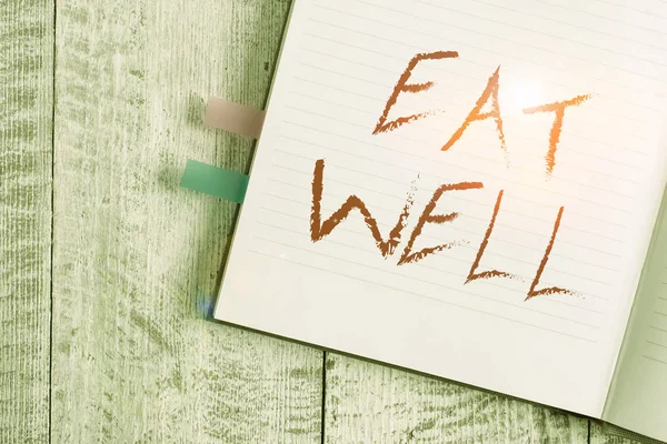 Writing note showing Eat Well. Business photo showcasing Practice of eating only foods that are whole and not processed Notebook stationary placed above classic wooden backdrop.