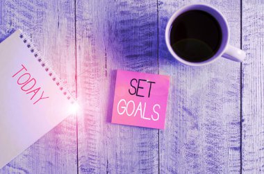 Set Hedeflerini gösteren kavramsal el yazısı. İş fotoğrafı metni gelecekte bir şey tanımlıyor ya da başarıyor. Tahta masanın üzerinde duran kahve fincanının yanına yerleştirilmiş plan sabit..