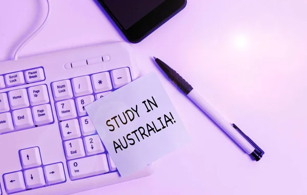 Handgeschreven tekst schrijven studie in Australië. Concept betekenis gaan in het buitenland orde Voltooi uw studies wit PC-toetsenbord met lege noot papier boven witte achtergrond. — Stockfoto