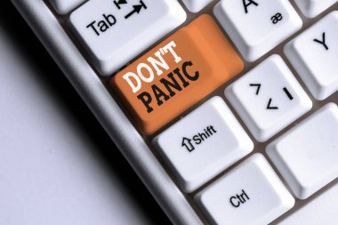 Don T Panic 'i gösteren bir not yazıyorum. Aniden ortaya çıkan iş fotoğraflarında güçlü bir korku hissi mantıklı düşünmeyi engeller. Beyaz bilgisayar klavyesi beyaz arkaplanının üzerinde not kağıdı ile birlikte..