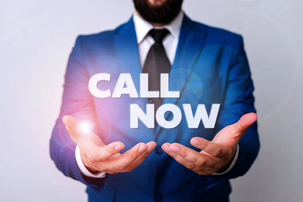 Signo de texto que muestra Call Now. Foto conceptual Para ponerse en contacto inmediatamente con una demostración utilizando dispositivos de telecomunicaciones con precisión Hombre con las manos abiertas en fron de la mesa. Teléfono móvil y notas sobre la mesa . —  Fotos de Stock