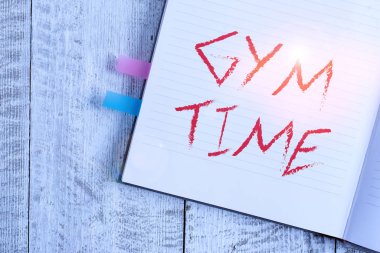 Jimnastik saatini gösteren bir not yazıyorum. İş fotoğrafı, egzersiz yapmaya başlamak için motivasyon gösteriyor. Formda kalmak için klasik ahşap zeminin üzerine yerleştirilmiş bir defter..