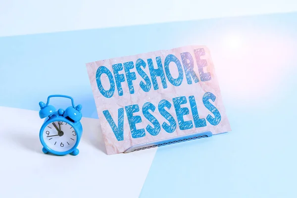 Az offshore hajók szöveges jele. A tengeri olaj- és gázfúrótornyok ellátására tervezett koncepcionális fotóhajó Mini méretű ébresztőóra egy pasztell hátterű papírlap mellett. — Stock Fotó