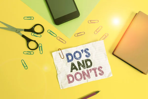 Text sign showing Do S And Don Ts. Conceptual photo Technologically complication of making a decision Paper sheets pencil clips smartphone scissors notebook colored background.