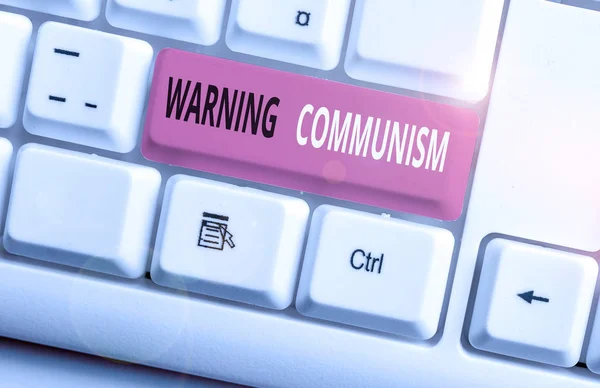 Conceptual hand writing showing Warning Communism. Business photo showcasing economic system where the group owns the production White pc keyboard with note paper above the white background.