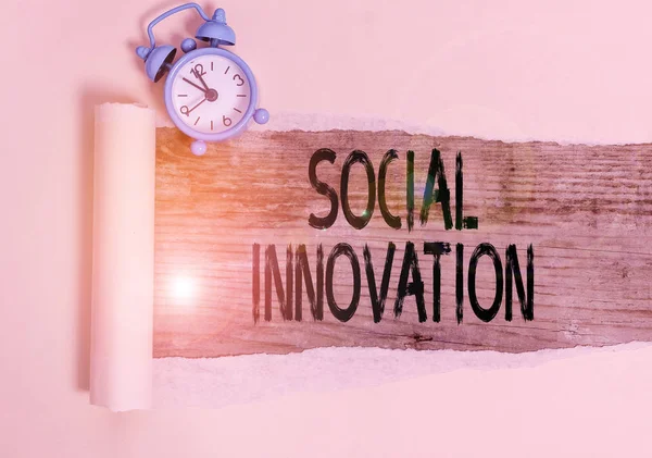 Text sign showing Social Innovation. Conceptual photo practices that aim to meet social needs in a better way Alarm clock and torn cardboard placed above a wooden classic table backdrop.