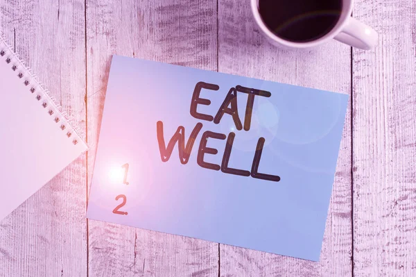 Handwriting text writing Eat Well. Concept meaning Practice of eating only foods that are whole and not processed Stationary placed next to a cup of black coffee above the wooden table.