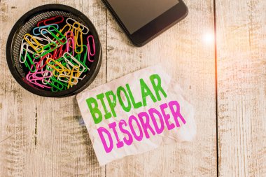 Bipolar bozukluk gösteren bir not yazıyorum. Ciddi yüksek ve düşük ruh halleri getiren iş fotoğraflarının sergilenmesi. Ahşap arka fonun üzerine yerleştirilmiş kağıt ve karton kırışıklıkları..