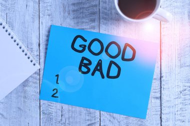 Handwriting text writing Good Bad. Concept meaning to seem to be going to have a good or bad result Life choices Stationary placed next to a cup of black coffee above the wooden table.