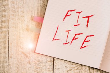 Fit Life 'ı gösteren bir not yazıyorum. İş fotoğrafı gösterimi, sağlıklı beslenme ve egzersizle ağırlığı muhafaza ediyor. Sağlıklı yaşayan bir not defteri, klasik ahşap zeminin üzerine yerleştirilmiş..