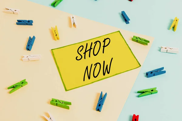 Word writing text Shop Now. Business concept for the action or activity of purchasing goods from stores or online Colored clothespin paper empty reminder yellow blue floor background office.