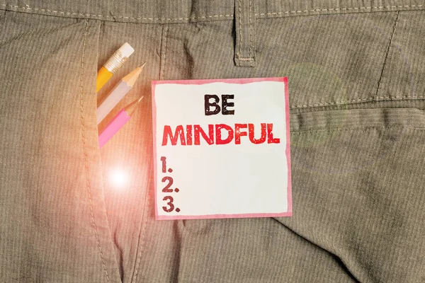 Writing note showing Be Mindful. Business photo showcasing paying close attention to or being conscious of something Writing equipment and blue note paper in pocket of trousers.