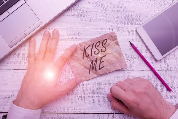 Writing note showing Kiss Me. Business photo showcasing informally request to touch my lips with your lips or press against Hand hold note paper near writing equipment and smartphone.