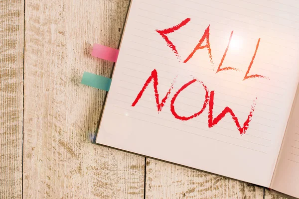 Writing note showing Call Now. Business photo showcasing To immediately contact a demonstrating using telecom devices with accuracy Notebook stationary placed above classic wooden backdrop.