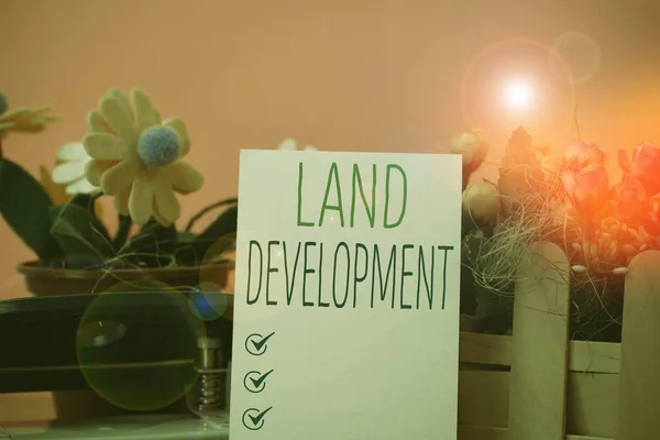Writing note showing Land Development. Business photo showcasing process of acquiring land for constructing infrastructures Flowers and writing equipments plus plain sheet above textured backdrop.
