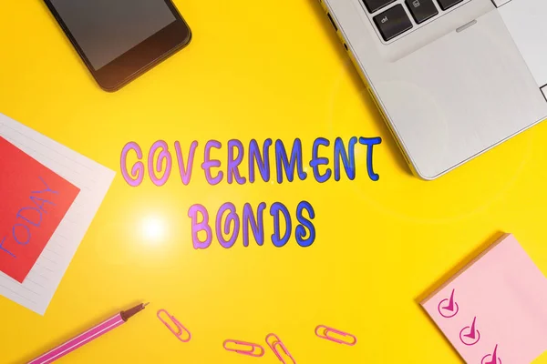 Text sign showing Government Bonds. Conceptual photo debt security issued by a government to support spending Laptop smartphone notepad marker paper sheet note clips colored background. — 스톡 사진