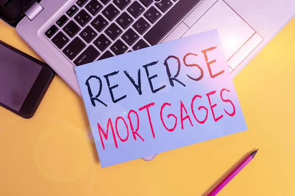 Writing note showing Reverse Mortgages. Business photo showcasing borrower to access the unencumbered value of the property Metallic laptop small paper sheet pencil smartphone colored background. — 스톡 사진