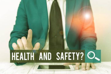 Sağlık ve Güvenlik Sorusu 'nu gösteren bir not yazıyorum. İş fotoğraflarında kaza ya da yaralanmayı önlemek için yönetmelikler ve prosedürler gösteriliyor. İşadamı parmağıyla onu işaret ediyor..