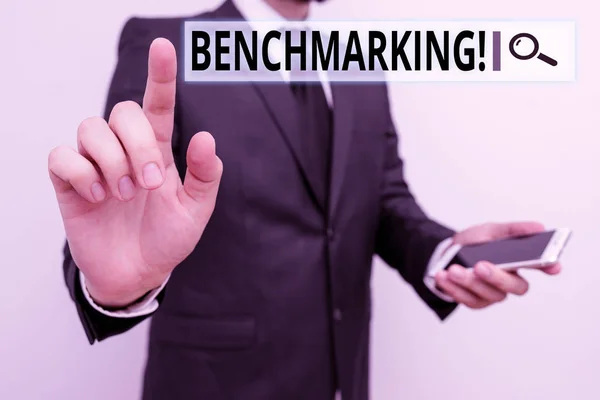 Nota de escritura que muestra Benchmarking. Exhibición de fotos de negocios evaluar algo en comparación con estándar o puntuaciones Hombre desgaste traje de trabajo formal mantener el teléfono inteligente con la mano . — Foto de Stock