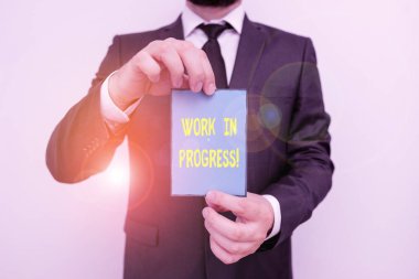Word writing text Work In Progress. Business concept for unfinished project that still added to or developed Male human wear formal work suit office look hold notepaper sheet use hand.