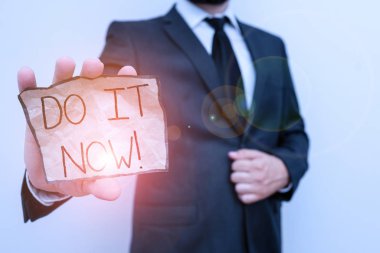Conceptual hand writing showing Do It Now. Business photo text not hesitate and start working or doing stuff right away Male human wear formal work suit with office look hold book.