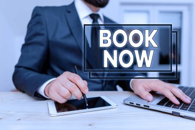 Writing note showing Book Now. Business photo showcasing Make a reservation in hotel accommodation or airplane ticket Male human wear formal clothes present use hitech smartphone.