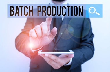 Toplu Yapım 'ı gösteren bir not yazıyorum. İş fotoğraflarının sergilendiği ürünler, grup olarak analiz edilir. Erkek insan resmi iş kıyafeti giyer. Akıllı telefon kullanır..