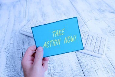 Take Action Now 'ı gösteren bir not yazıyorum. İş fotoğrafı sergisi resmi bir şey yap ya da uyumlu bir şey. Elinde renkli hatırlatıcı kare şeklindeki kağıt ahşap zemin tutan adamla sorunlara odaklan..