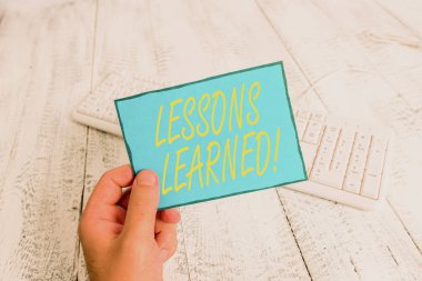 Writing note showing Lessons Learned. Business photo showcasing experiences distilled project that should actively taken Man holding colorful reminder square shaped paper wood floor. clipart