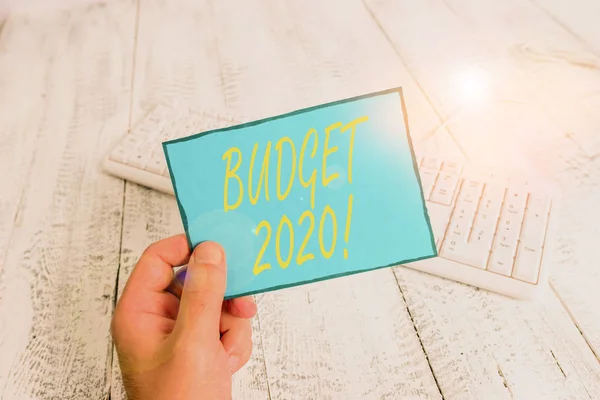 Writing note showing Budget 2020. Business photo showcasing estimate of income and expenditure for next or current year Man holding colorful reminder square shaped paper wood floor.