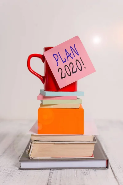 Conceptual hand writing showing Plan 2020. Business photo showcasing detailed proposal doing achieving something next year Cup sticky note stacked note pads books box wooden table.