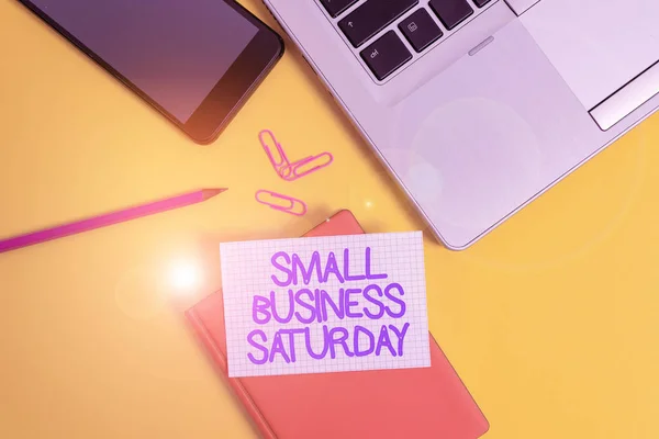 Conceptuele handschrift tonen Small Business zaterdag. Zakelijke foto presentatie Amerikaanse shopping vakantie gehouden tijdens de zaterdag Laptop smartphone clip potlood papier vel gekleurde achtergrond. — Stockfoto