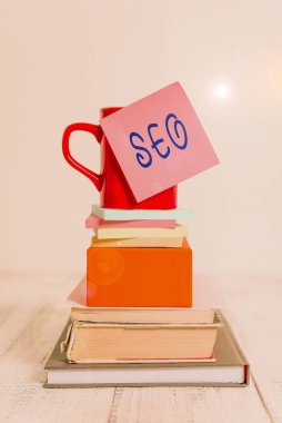 Seo 'yu gösteren kavramsal el yazısı. İş fotoğraflarınız, internetteki iş yerinizi pazarlamanın inanılmaz etkili bir yolunu gösteriyor. Kupa yapışkan notu, not defterleri, kutular, ahşap masa..