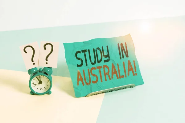 Avustralya 'da Çalışmayı gösteren kavramsal el yazısı. Yabancı ülke düzenine giren iş fotoğrafı sergisi eğitiminizi tamamlıyor. Pastel arka plana yerleştirilmiş kağıdın yanında çalar saat.. — Stok fotoğraf