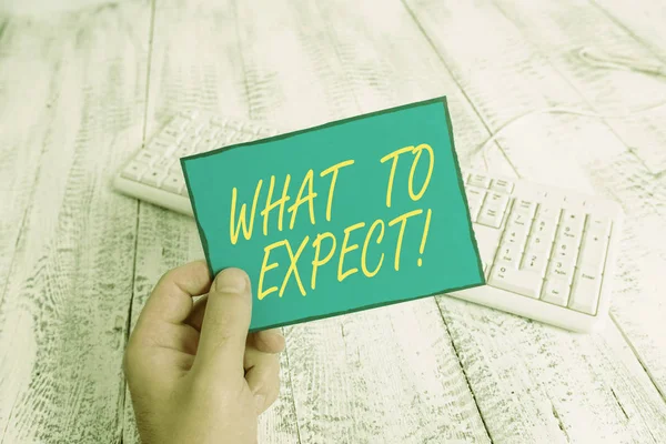 Writing note showing What To Expect. Business photo showcasing asking about regard something as likely to happen occur Man holding colorful reminder square shaped paper wood floor. — Stockfoto