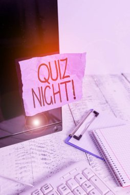 Quiz Night 'ı gösteren bir not yazıyorum. Klavye yakınındaki siyah bilgisayar ekranına yapıştırılmış not kâğıdı ve durağan bireyler arasındaki akşam testi bilgi yarışmasını gösteren iş fotoğrafı.